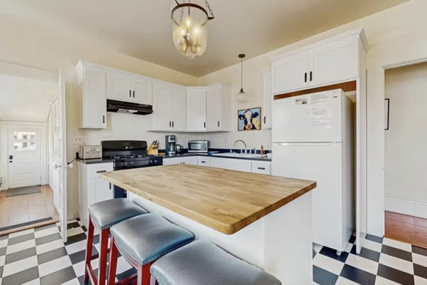 Modern kitchen with white cabinetry, black gas range, wood countertop island with red stools, and checkered floor.